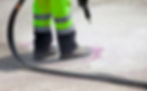 Worker in high-visibility clothing uses a spray gun on a road surface