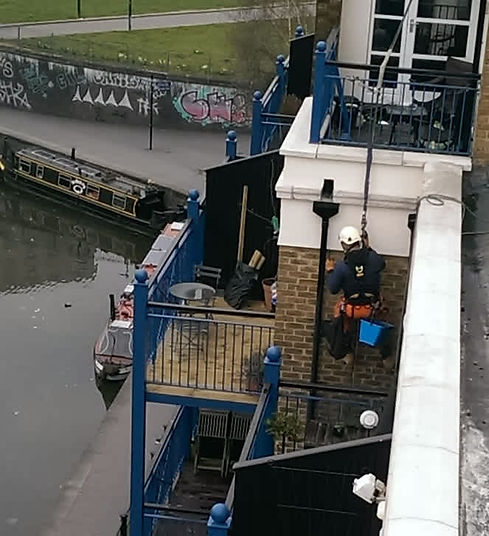 workers secured by a rope on the side of a building cleaning gutter 
