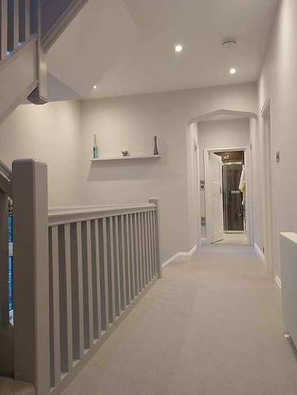 Bright hallway with white walls and carpet, featuring a staircase on the left.