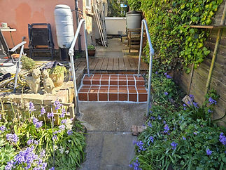 A garden pathway with red tiled steps leading to a patio