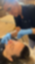 A professional aesthetician in a black uniform and blue gloves performs a cosmetic lip filler injection on a client lying on a clinical treatment bed.
