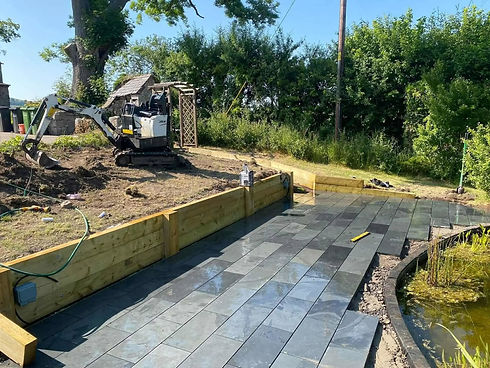 A small excavator sits on a dirt area beside a newly laid slate patio