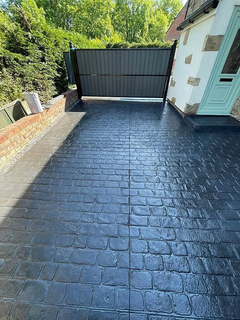 A paved driveway with a glossy, wet look leads to a closed wooden gate