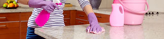 Person in striped shirt, wearing purple gloves, cleans a countertop with a pink spray and cloth