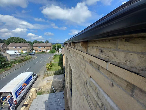 View from a roof showcasing newly installed black gutters on a stone building.