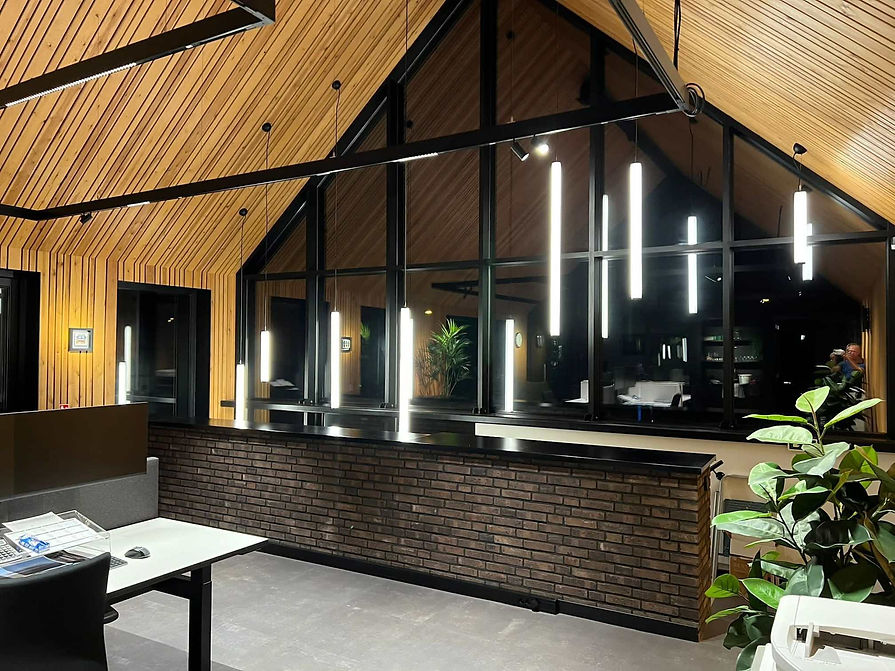 Modern office interior with wood-paneled vaulted ceiling, hanging vertical lights, brick h