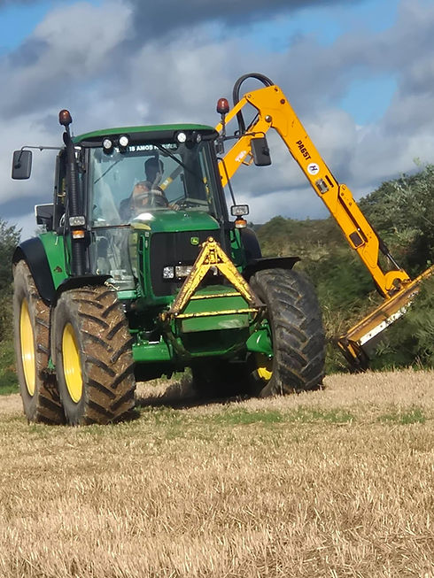 a tractor with a mechanical arm trimming hedges in field