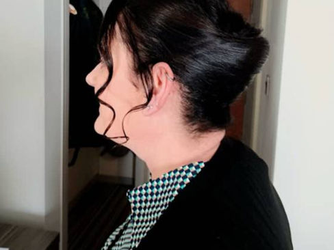 Profile view of a woman with a sleek, dark updo and curled strands framing her face