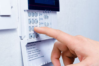 A hand pressing buttons on a wall-mounted security alarm keypad