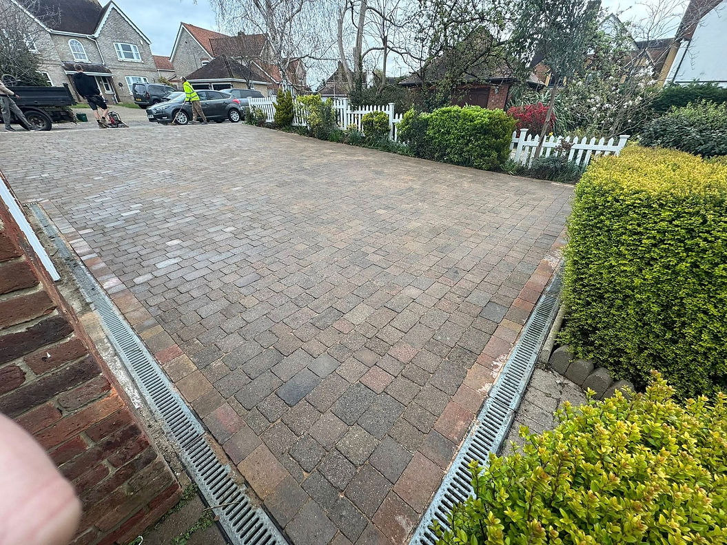 Brick driveway with drainage, bordered by lush green hedges and a white picket fence_