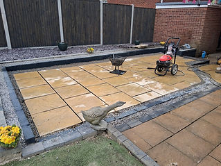 Backyard patio with large beige pavers surrounded by dark stone edging and gravel.