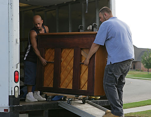 Two men carefully load a large piano into a moving truck using a ramp