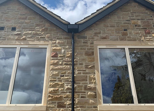 A symmetrical stone house facade with large windows and black gutter pipe