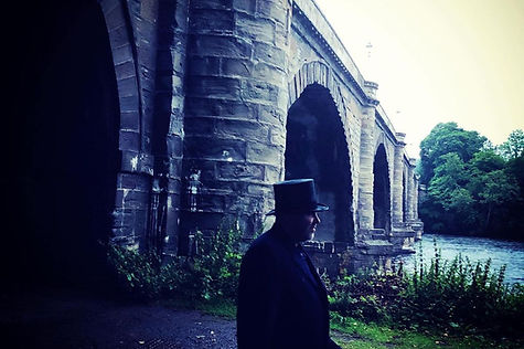 Man in top hat in front of bridge