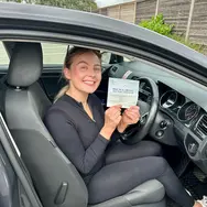 a woman sitting in car showing her certificate while posing for the camera