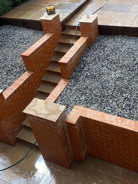 split level garden with central steps surrounded by brick retaining walls and gravel beyond