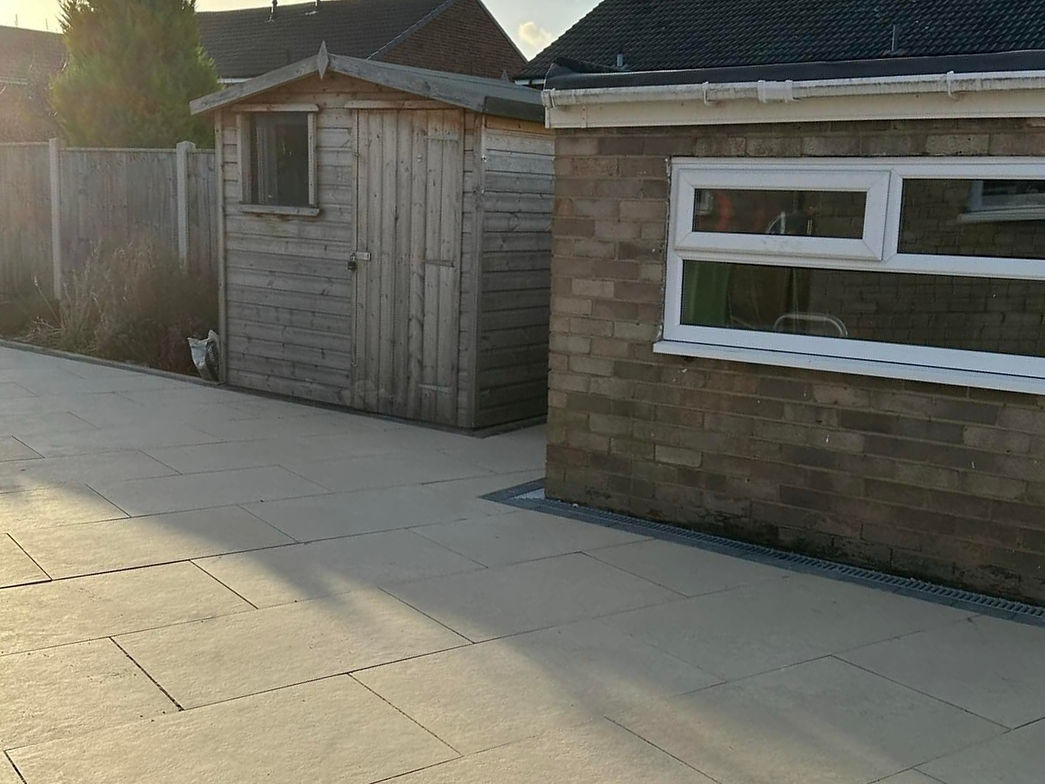 Modern stone patio leading to a wooden shed and fence