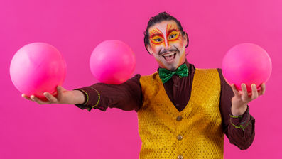 להטוטן מחייך מבצע ג’אגלינג בכדורים ורודים על רקע צבעוני