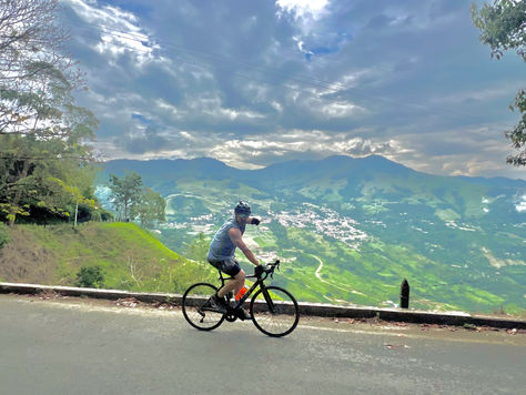 Clay Martin biking in helmet rides on mountain road with green hills and town below.