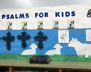 An example of one of the bulletin boards we use for Children's Church on Sundays. It says "Psalms for Kids" and has 3 crosses crafted from cardboard and cutouts of lambs and a donkey.