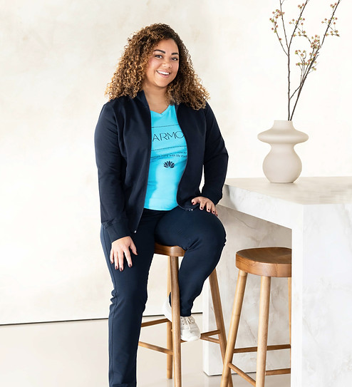 Volslanke curvy dame zit blij en comfortabel op kruk in blauwe Silvermedal damesjogging in grote maat