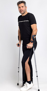 Heer stapt met krukken in revalidatiebroek met rits opzij na knieoperatie