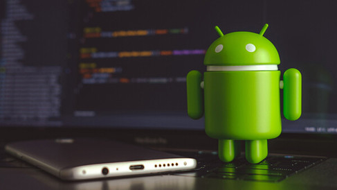 Dans l'image, on peut voir une figurine verte d'un robot Android se tenant à droite d'un ordinateur portable avec un écran flou affichant du code ou des informations système. L'ordinateur portable est posé sur une surface réfléchissante et un câble USB y est branché. L'arrière-plan est sombre, mettant en valeur la couleur verte vive du robot et de l'ordinateur portable. Représentant du Code Unity qui fonctionne sur la plateforme Android.