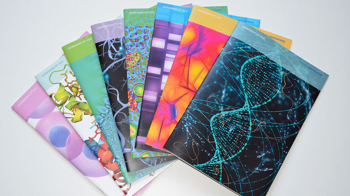 Acht gedruckte bunte Jahresberichte liegen aufgefächert zur Ansicht bereit.
