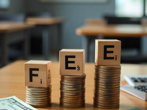 Stacked coins with wooden letter blocks spelling 'FEE', placed beside dollar notes and an Indian passport on a classroom desk, symbolizing rising student visa costs for international students in Australia.