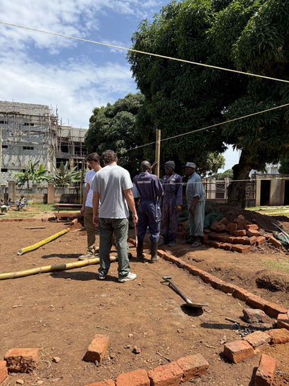 A group of Grace Place Volunteers collaborate on the cleared site, surrounded by bricks and tools, as they plan the initial phases of the Walipini Impact Build, emphasizing the collaborative Walipini Impact in Uganda.	