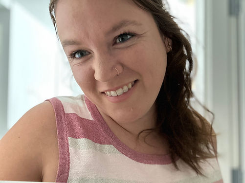 Picture of Lizzie (brunette white woman) looking to the left and smiling at the camera. She is wearing a glittery pink and silver striped top.