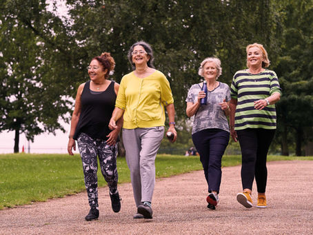 Four women walking along a path in a park, with trees behind them.