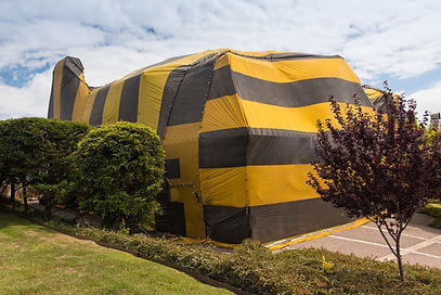 Large residential home covered with a striped fumigation tent for termite treatment