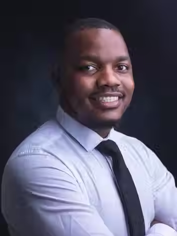 Professional male business headshot of a smiling man wearing a white shirt and black tie on a dark studio background.