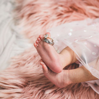 Baby feet with wedding rings — Close-up of newborn baby feet with parents’ wedding rings resting on tiny toes, symbolising love and family connection during a newborn photography session.
