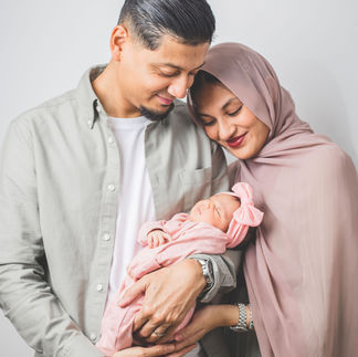 Family cuddling newborn — The Mustaq family holding their baby together, smiling warmly for a relaxed portrait captured with natural lighting during an in-home family photoshoot in Chester.