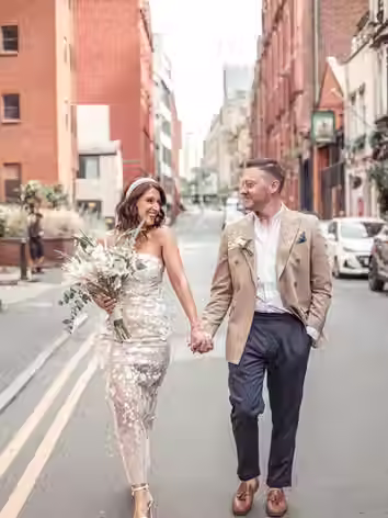 Urban wedding photography of a newlywed couple walking happily down a city street holding hands
