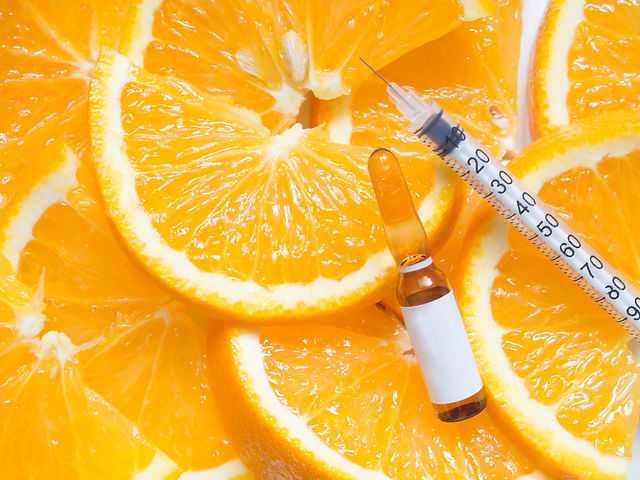 High dose vitamin C brown ampule for injection with syringe on fresh juicy orange fruit sl