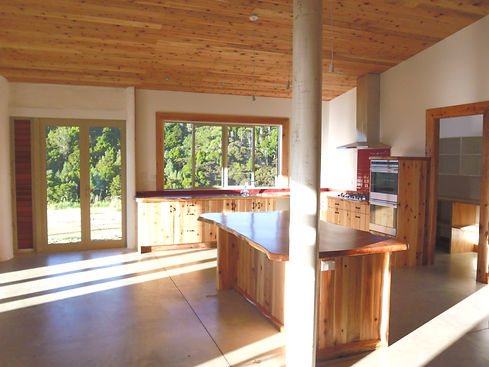 A custom wooden kitchen with wooden slab benchtops and high end finish, in an eco-friendly home overlooking New Zealand bush in Northland Whangarei. Straw bale, adobe mud brick and white plaster were used in the construction.