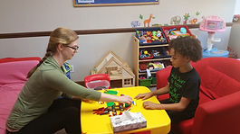 A woman and a child sit in a counseling room playing with toys