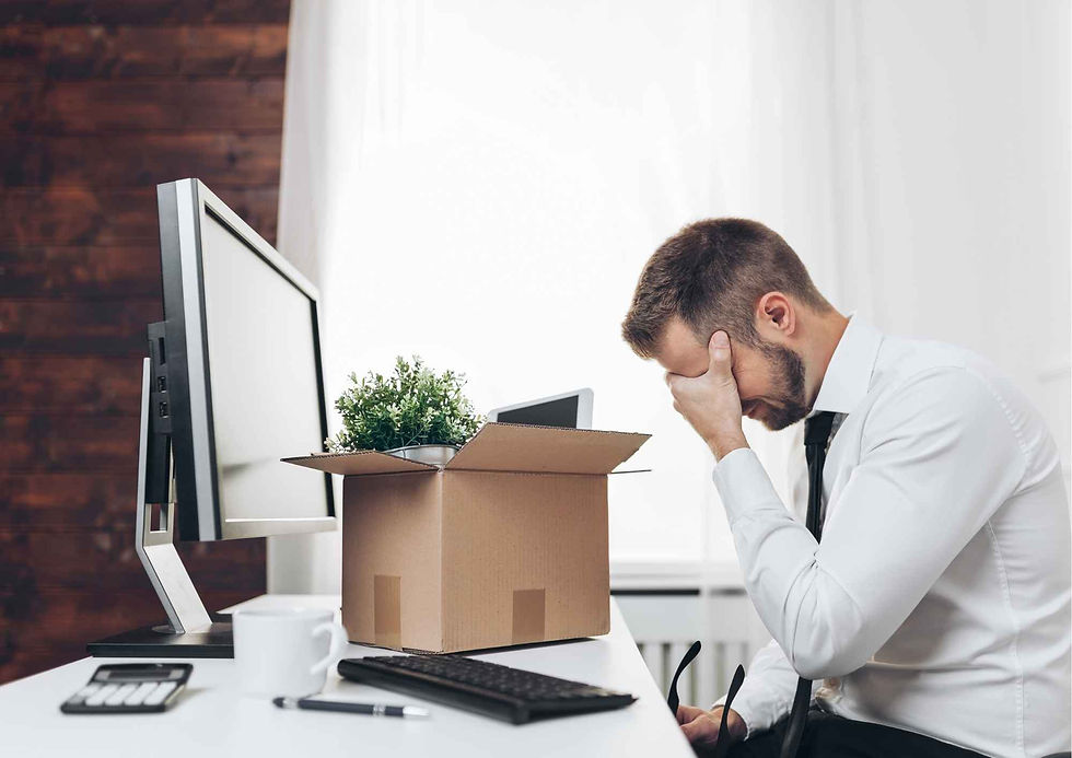 A despairing Employee holds his head in his hand at his desk after redundancy news breaks out
