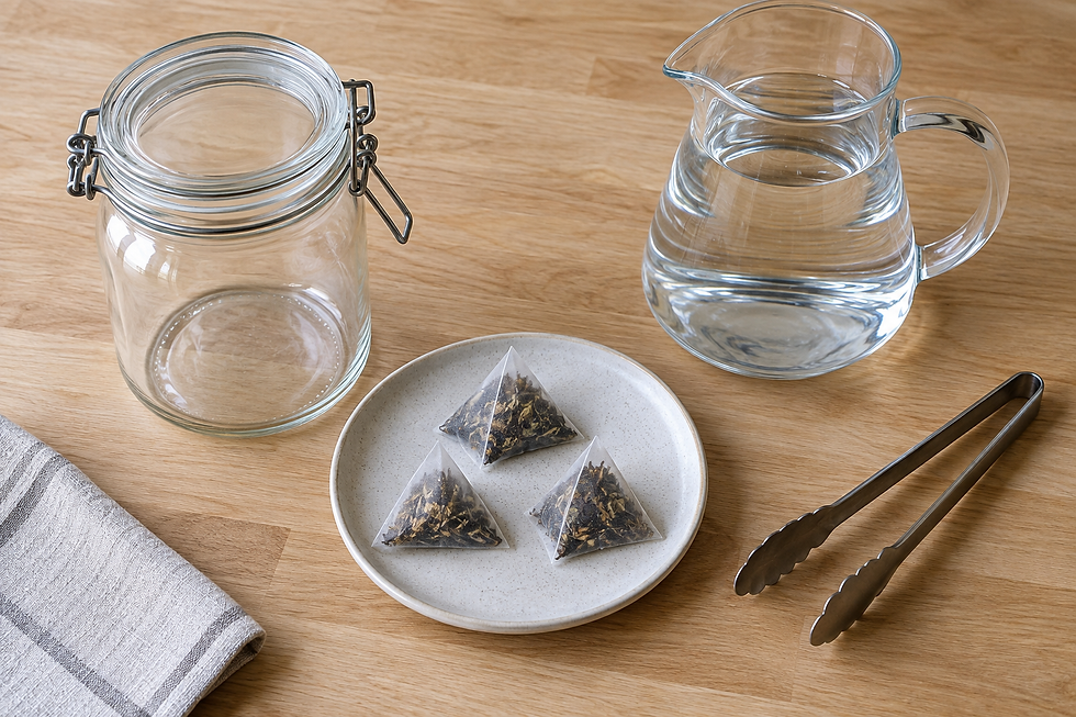 Clean cold-brew setup with an empty lidded jar, water carafe, tongs, and three sealed, stringless pyramid sachets.