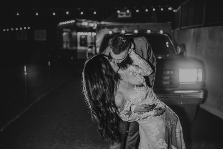 black and white image of groom kissing bride while dipping her in front of truck lights
