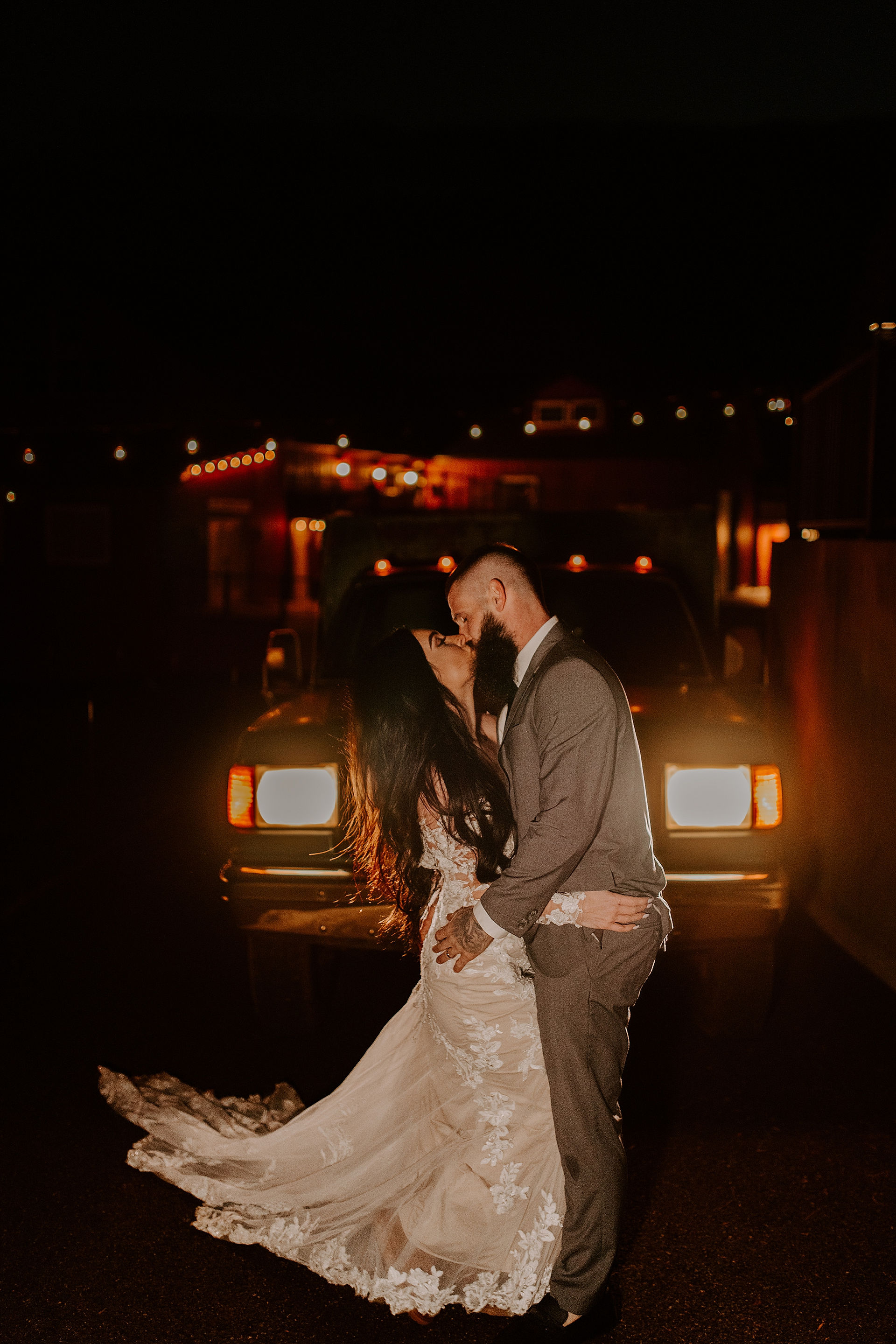 bride and groom kissing in front of truck lights in the dark