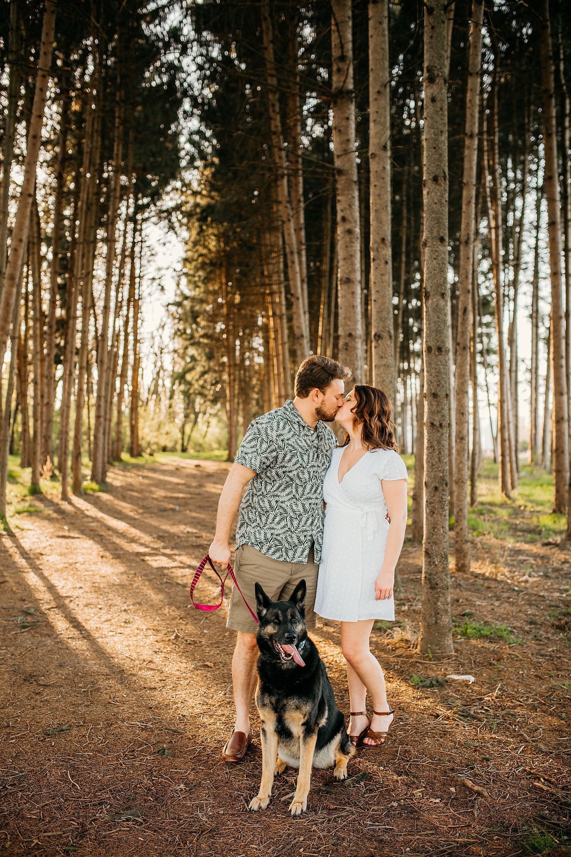 Couple kissing in woods with their dog