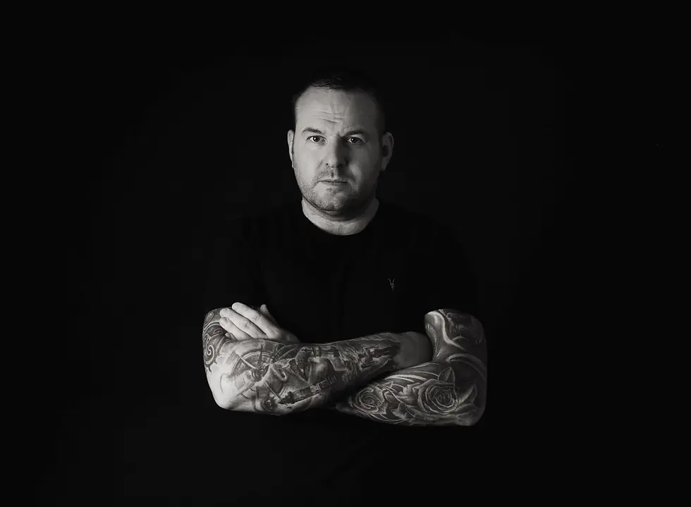 Black-and-white portrait of Northern Irish DJ and producer Eddie-B standing with crossed arms, representing his Progressive House, underground House and Techno sound.
