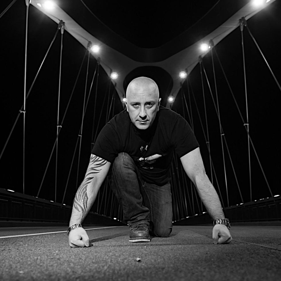 German DJ and producer Frank Savio kneeling on a bridge at night with one foot forward with his hands in fists touching the ground, black and white image.
