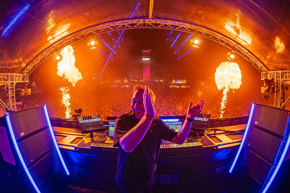 Electronic music artist Paul van Dyk performing on stage at a large festival crowd during a high-energy live show featuring flames, colourful lighting and an open-air arena atmosphere.