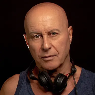British DJ and producer Graham Gold in a studio portrait wearing Sennheiser HD25 headphones around his neck against a dark background.