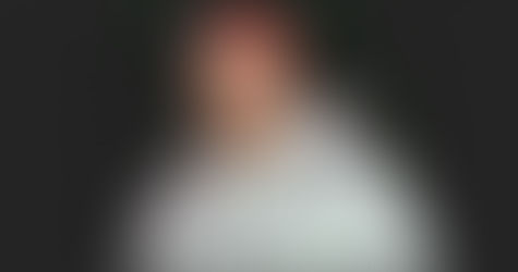 Italian DJ and producer Daniel Kaiser Malengo standing wearing a grey hoodie and red bandana on his head looking at the camera, colour image with black background